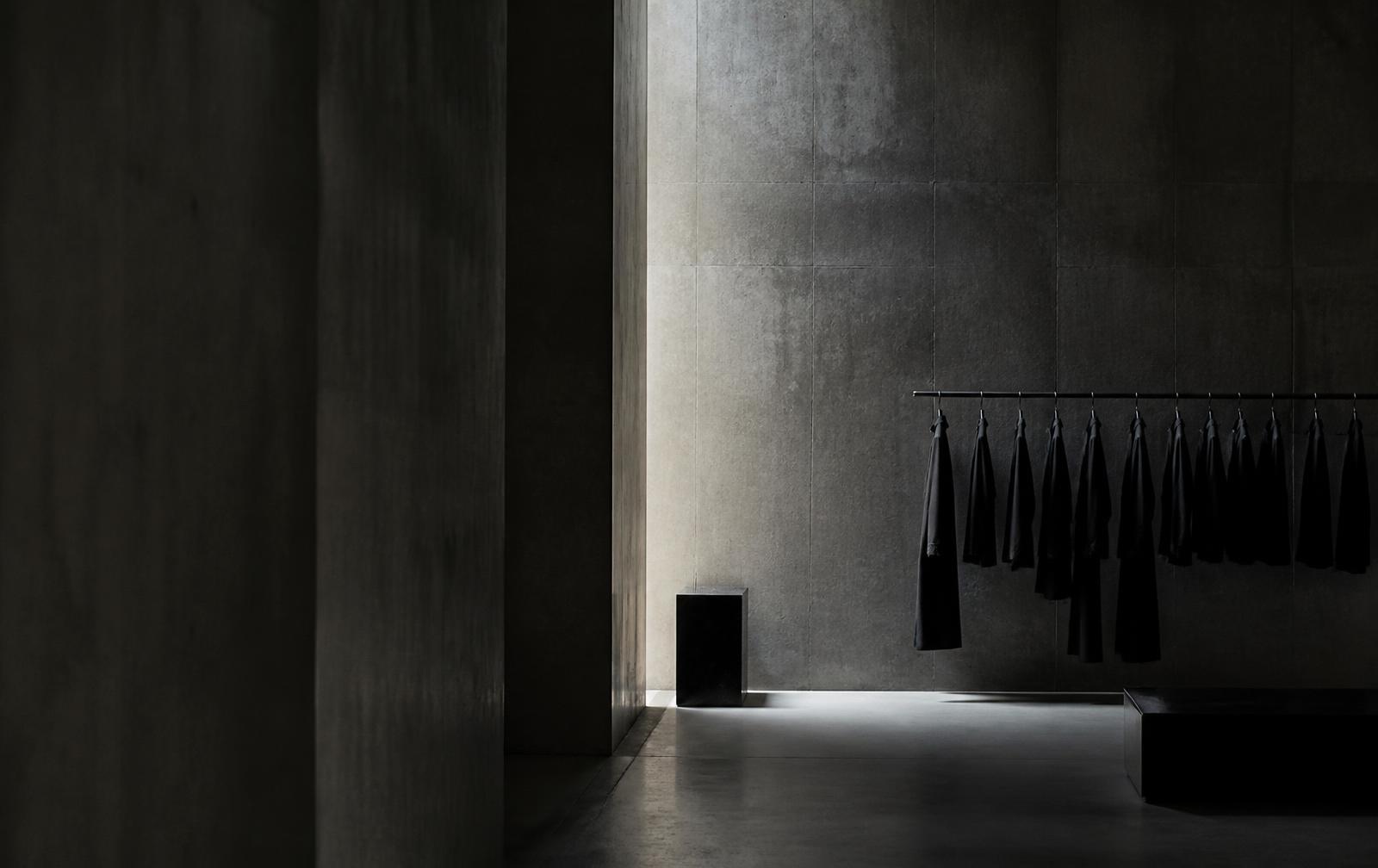 A dark concrete showroom with a rail of black garments