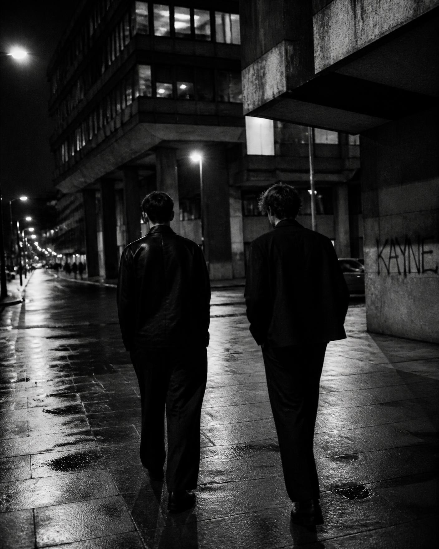 Two friends walking a wet city street late at night
